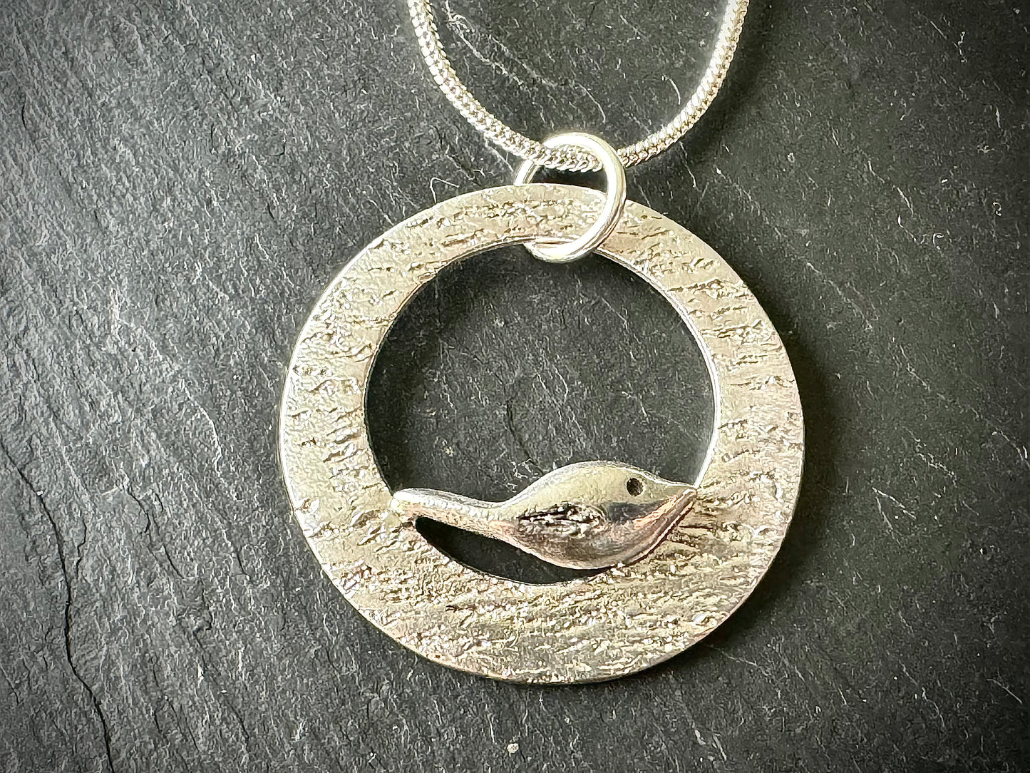 Handmade silver bird perching on silver rippled circle necklace