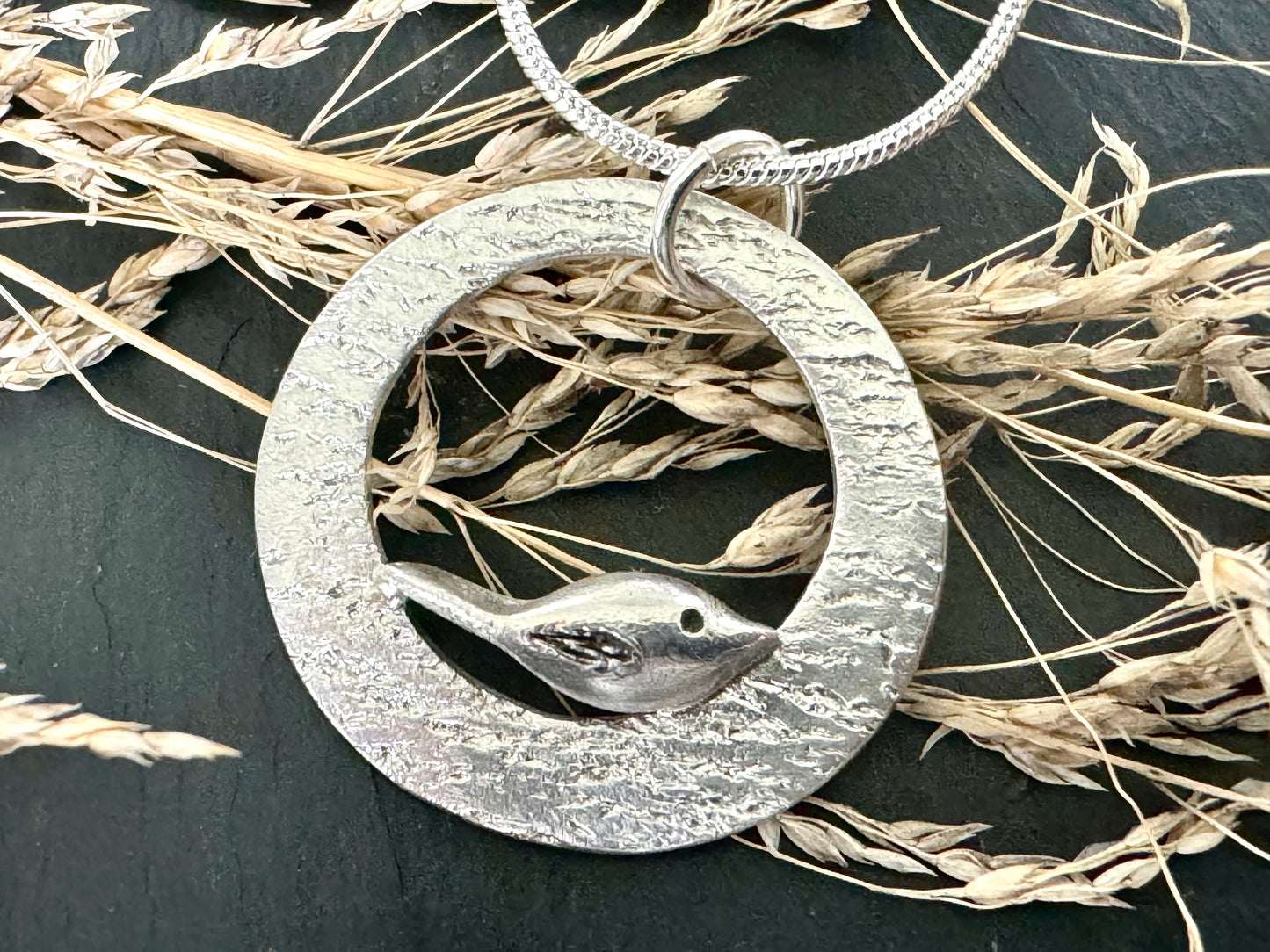 Handmade silver bird perching on a silver circle with ripple effect. Pendant necklace