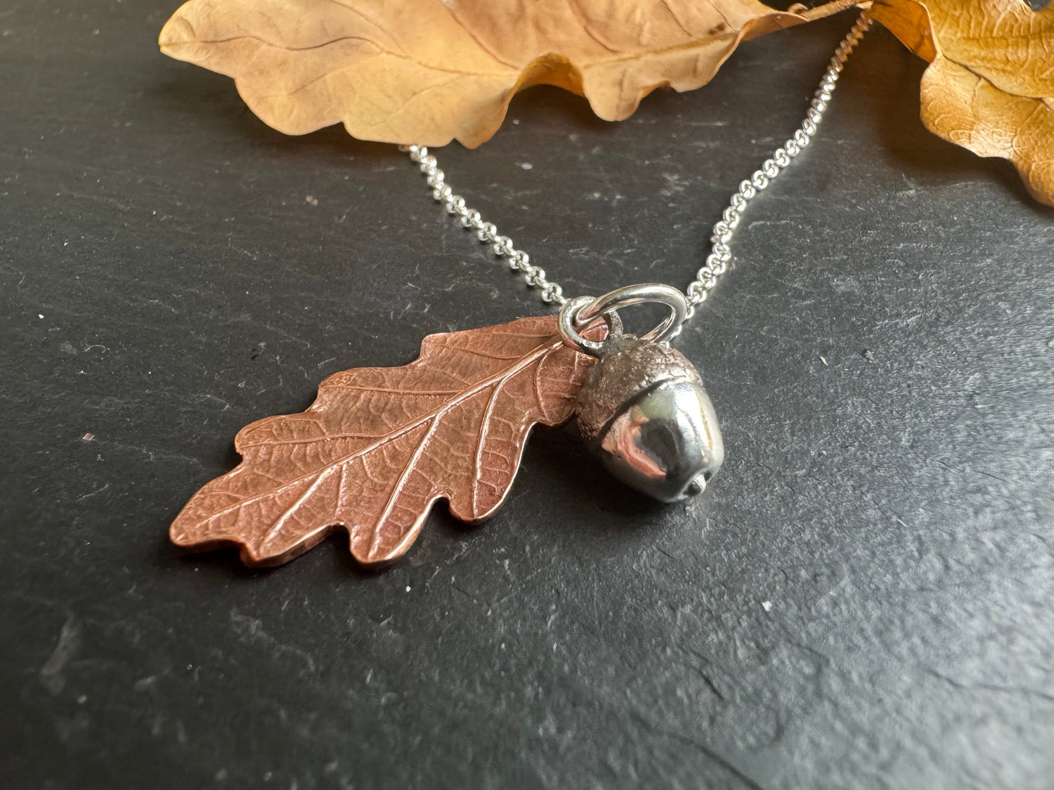 A copper oak leaf and silver acorn pendant on a silver chain 