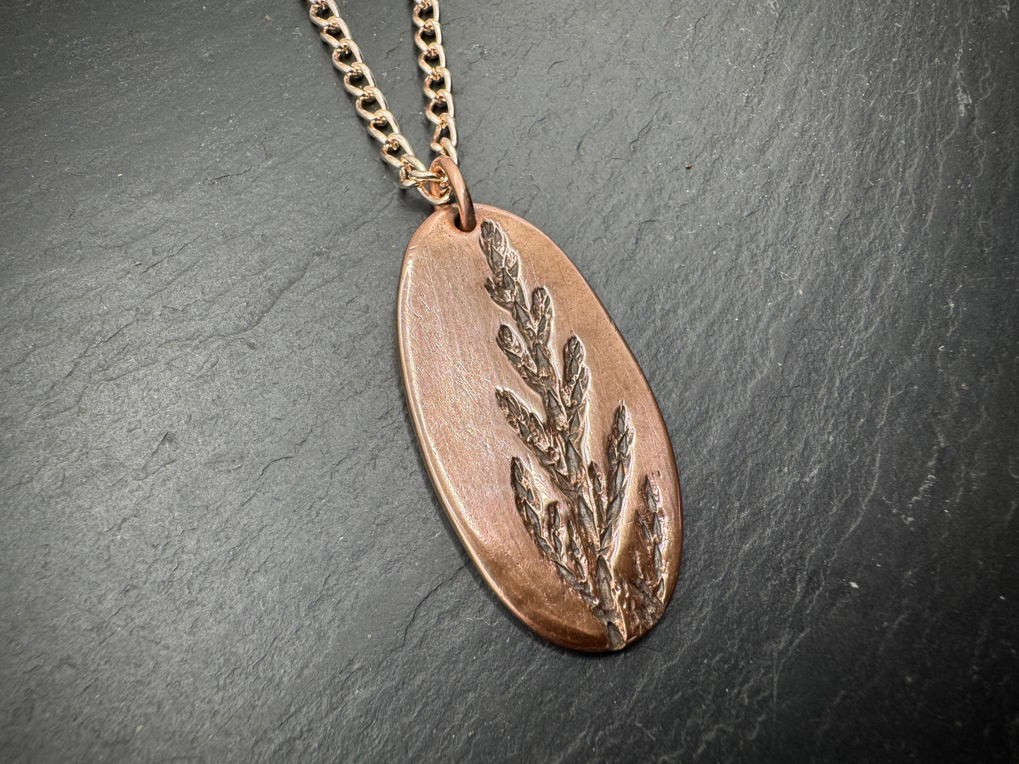Copper pendant necklace with leaf design on a dark surface