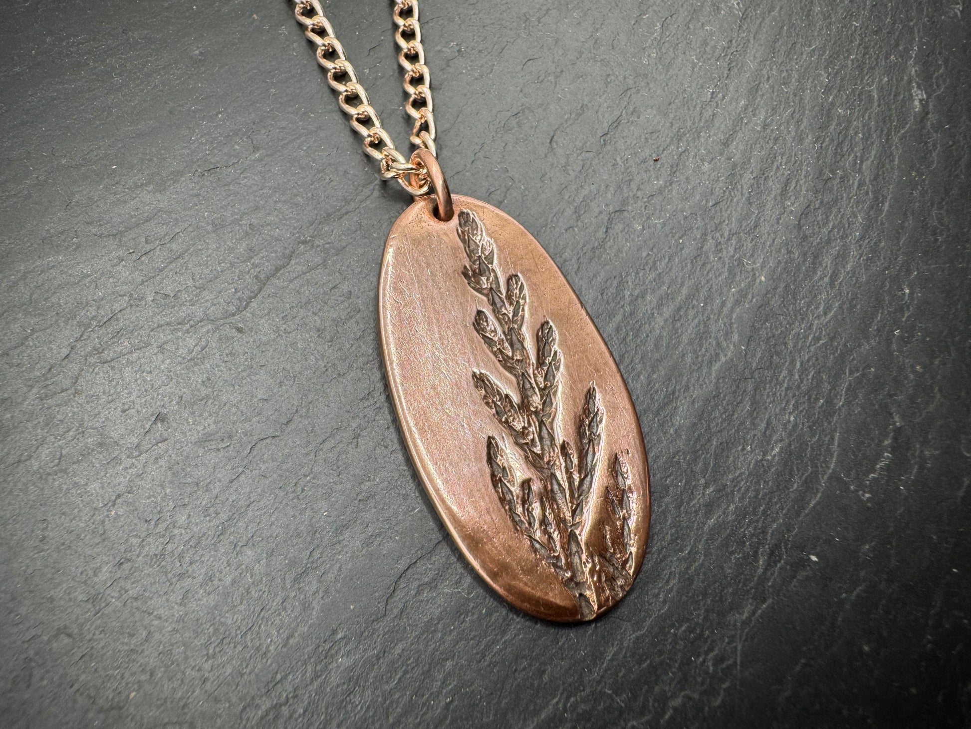 Copper pendant necklace with leaf design on a dark surface