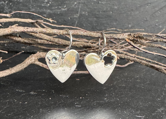 Heart-shaped silver earrings on a dark surface with twigs.