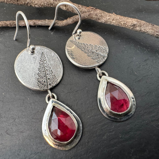 Silver earrings with red garnet teardrop stones on a dark surface