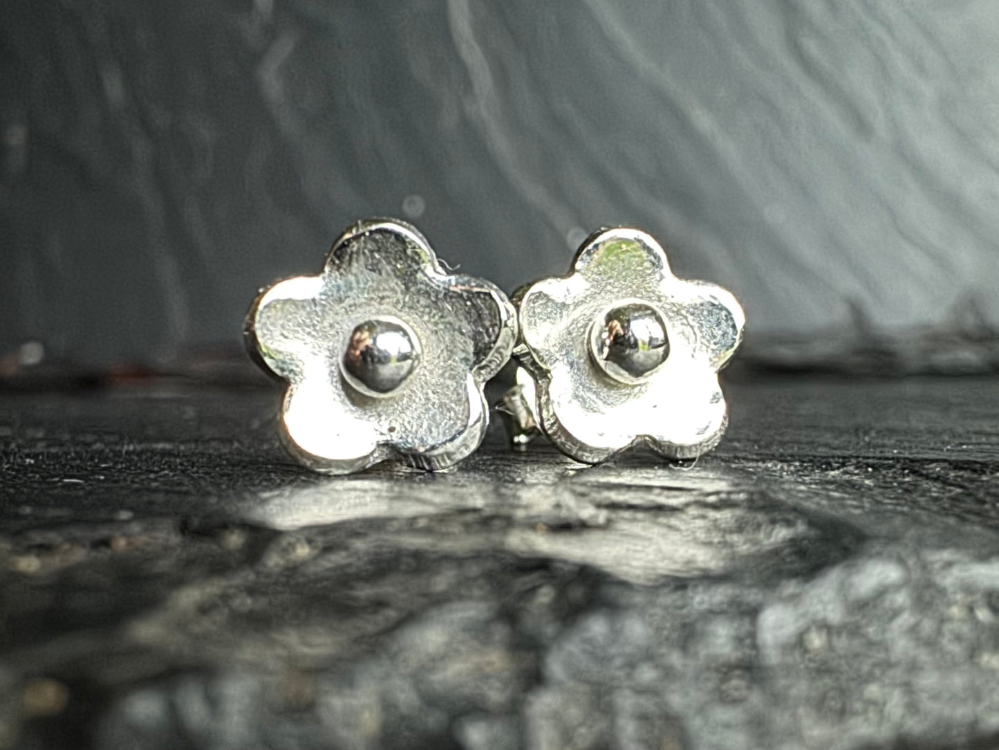 Silver flower-shaped earrings on a textured dark surface
