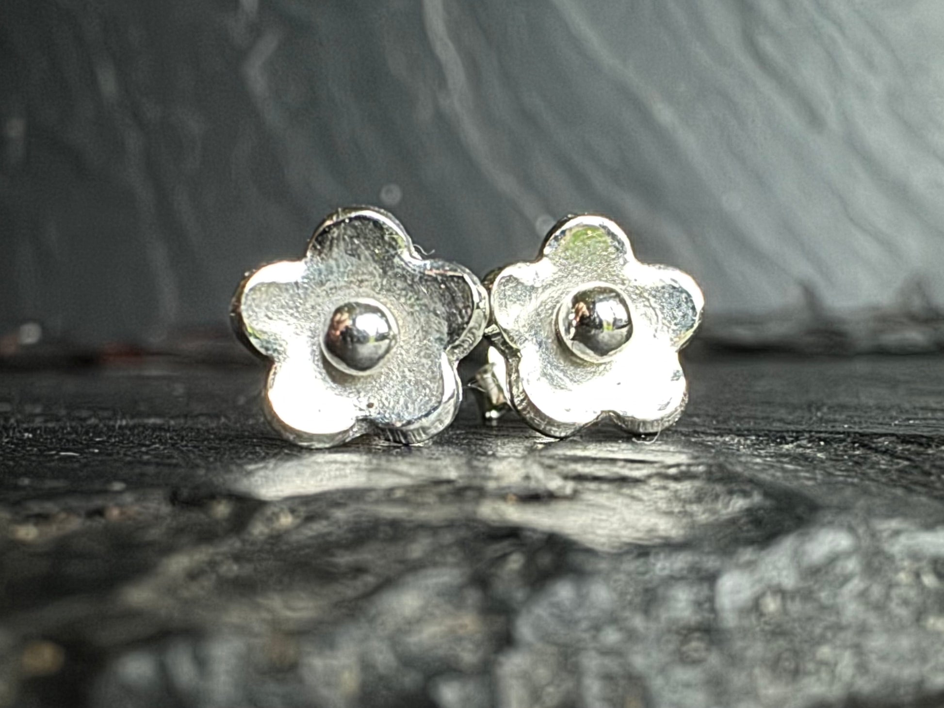 Silver flower-shaped earrings on a textured dark surface