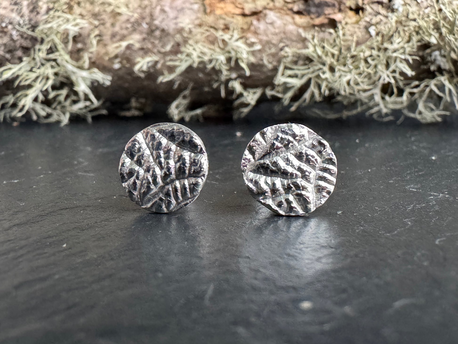 Pair of silver round earrings on a dark surface with a natural background