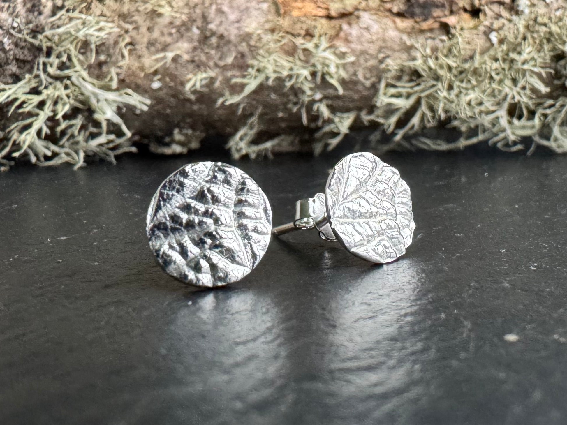 Silver leaf-patterned earrings on a dark surface with a natural background