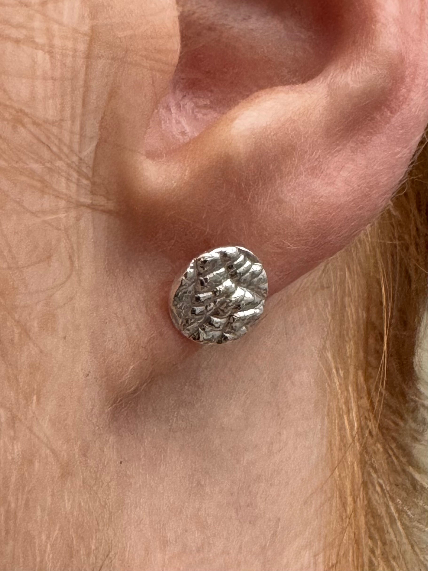 Silver textured earring on a person's ear