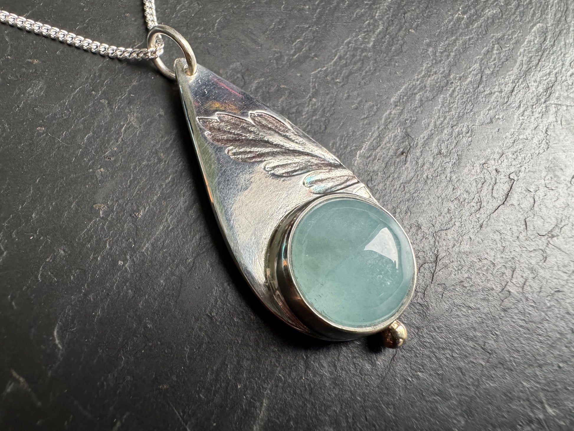 Silver pendant with a light blue gemstone on a dark surface