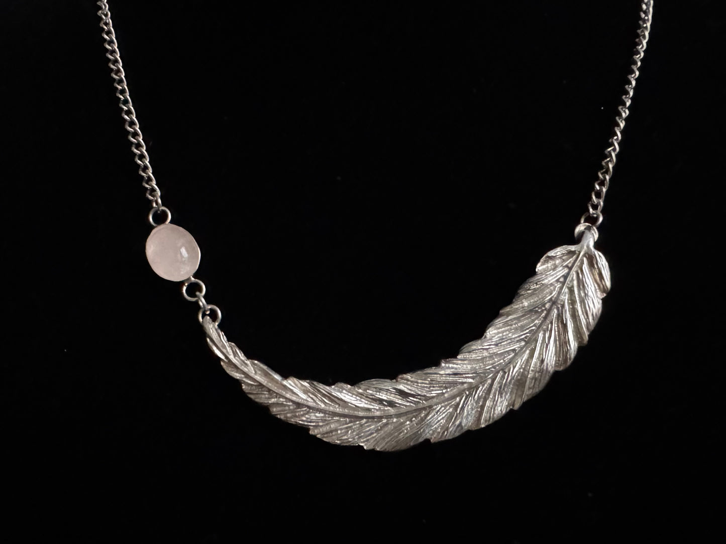 Silver feather-shaped pendant on a chain against a black background